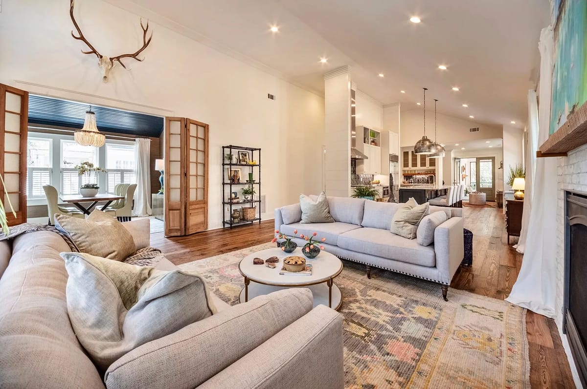 Living room with gray sectional sofa, white coffee table, area rug, bookshelves, and plants.