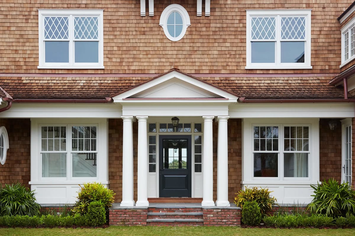 Exterior front of a house with columns, shingle walls, and landscaped plants