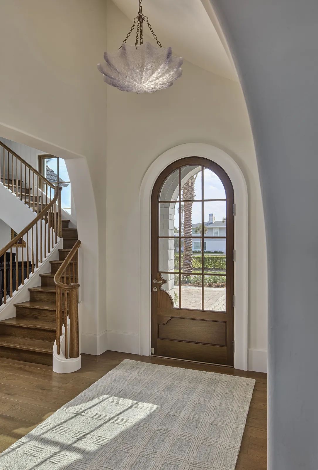 Foyer with wooden front door, cream rug, arched doorway, and curved staircase with wooden railings