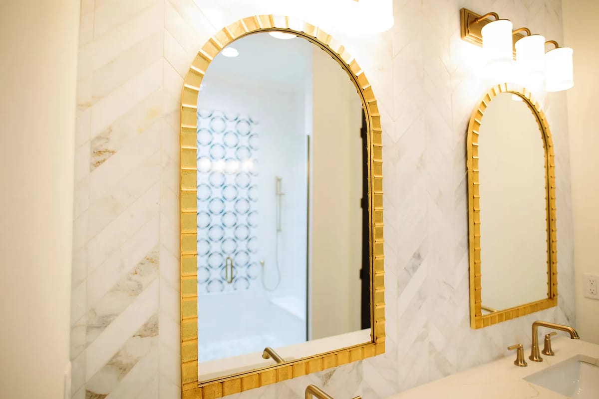 Bathroom with dual gold-framed mirrors, marble countertop, installed faucets, and a patterned shower curtain