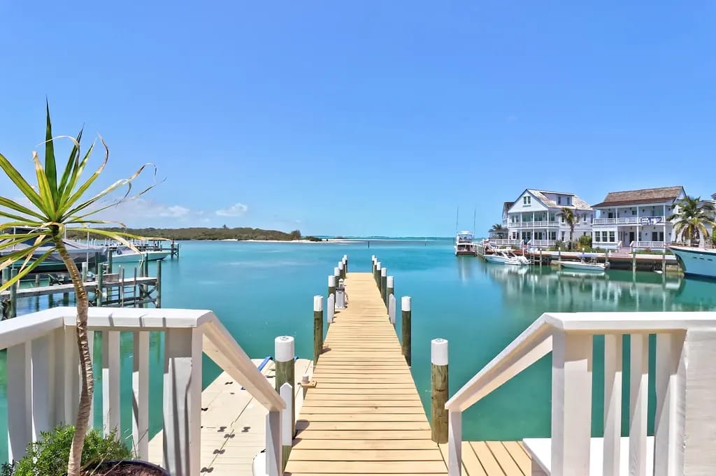 Outdoor deck overlooking water with walkway, boats, and waterfront houses.