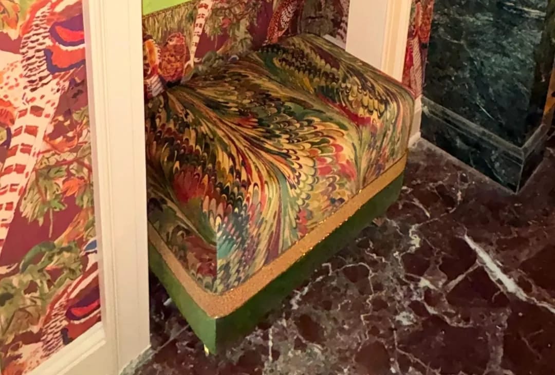 Small seating area with colorful bench and vibrant patterned wallpaper against a marbled tile floor.