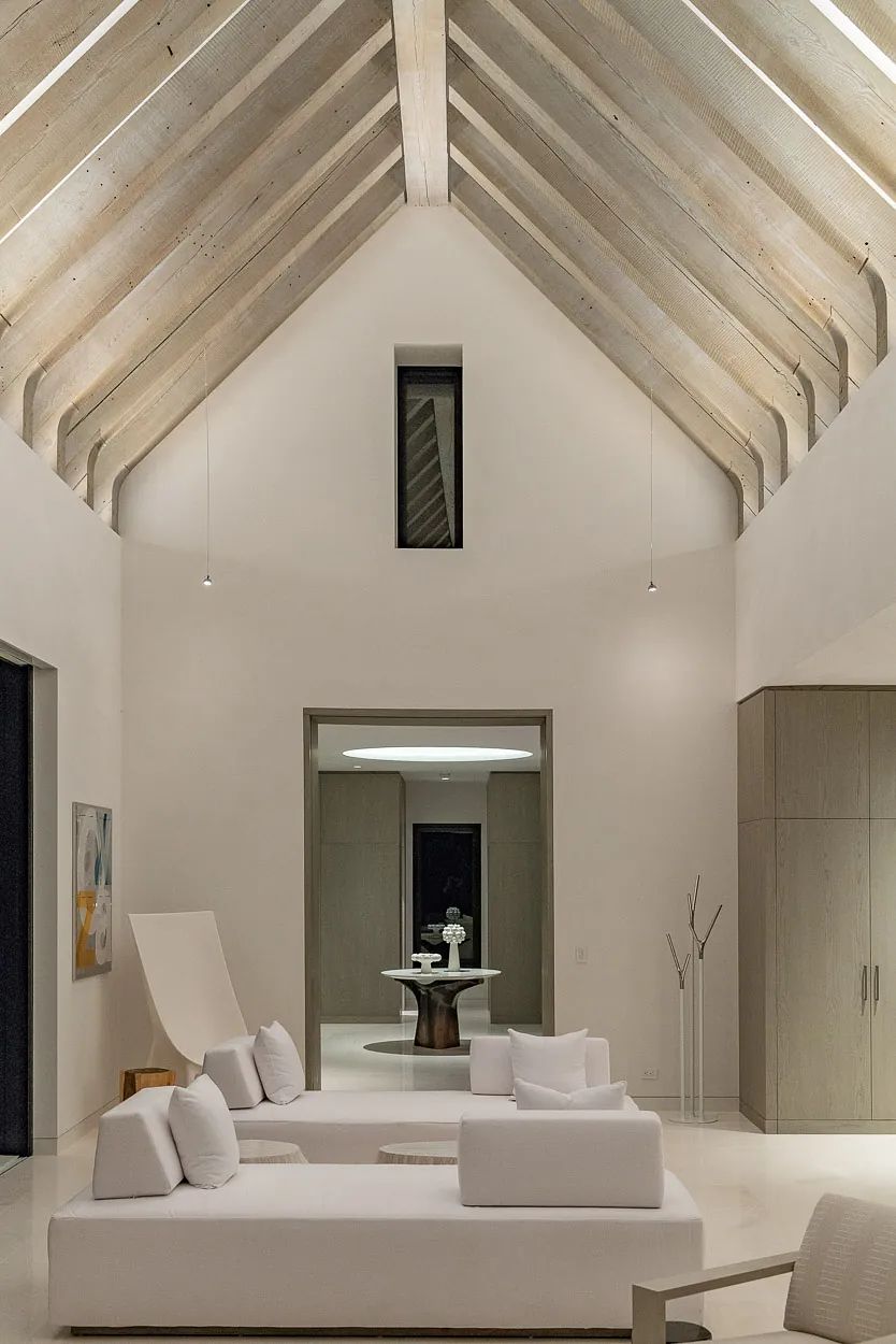 Living room with white sofas, light coffee table, area rug, wooden beams, and decorative sculpture in the corner