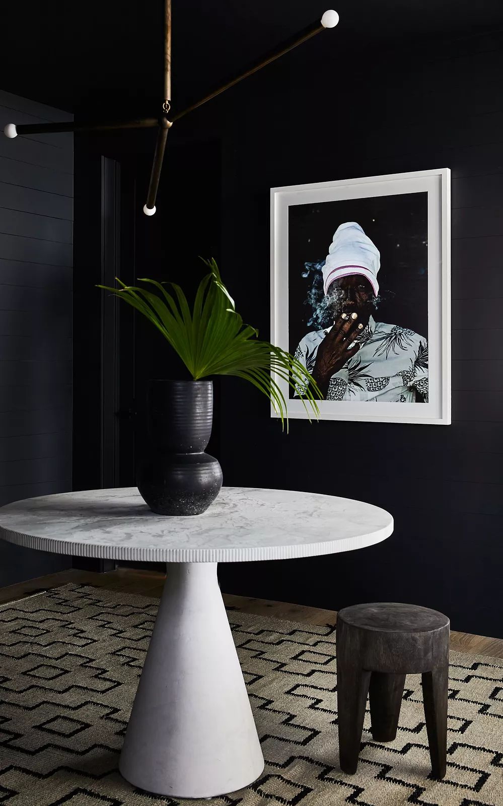 Small space with round marble table, black stool, plant, and artwork on the wall.