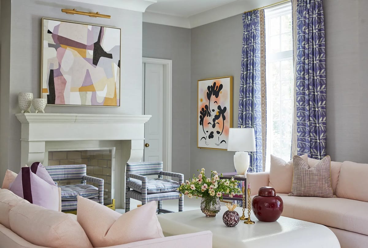 Living room with pink sofa, white coffee table, patterned armchairs, fireplace, and artwork on light gray walls.