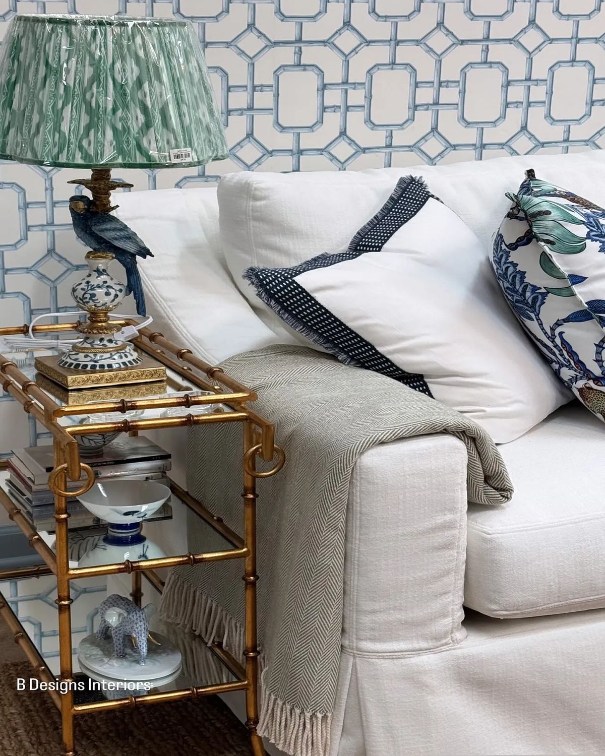 Living room with white sofa, gold side table, green lamp, patterned cushions, and decorative wallpaper.