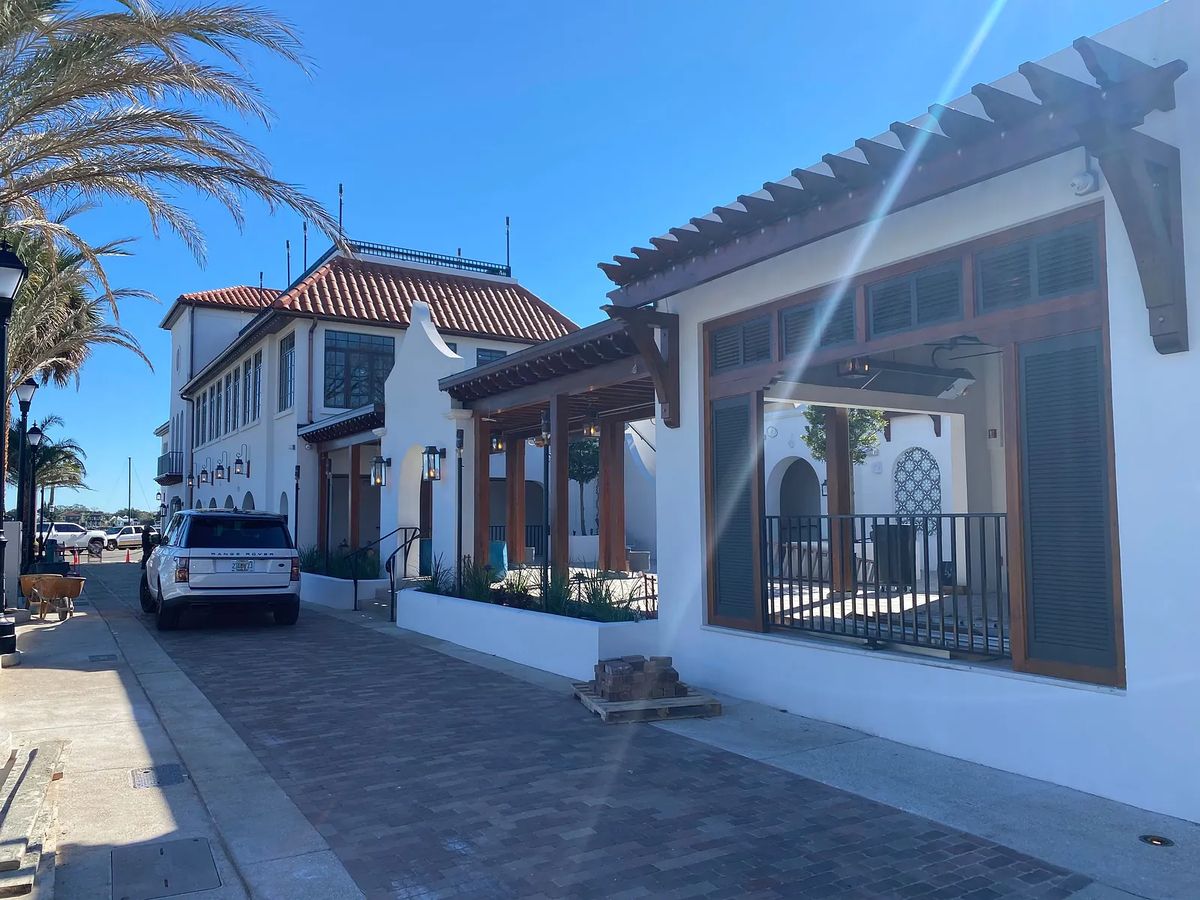 Exterior front view of a two-story building with tile roof, wooden beams, palm trees, and a brick pathway.