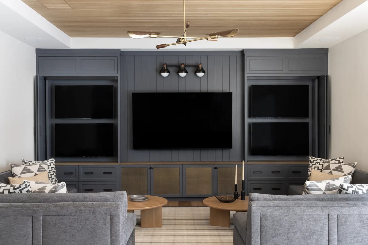 Living room with gray sofas, coffee tables, area rug, wall-mounted TV, built-in cabinetry, and wood paneling.