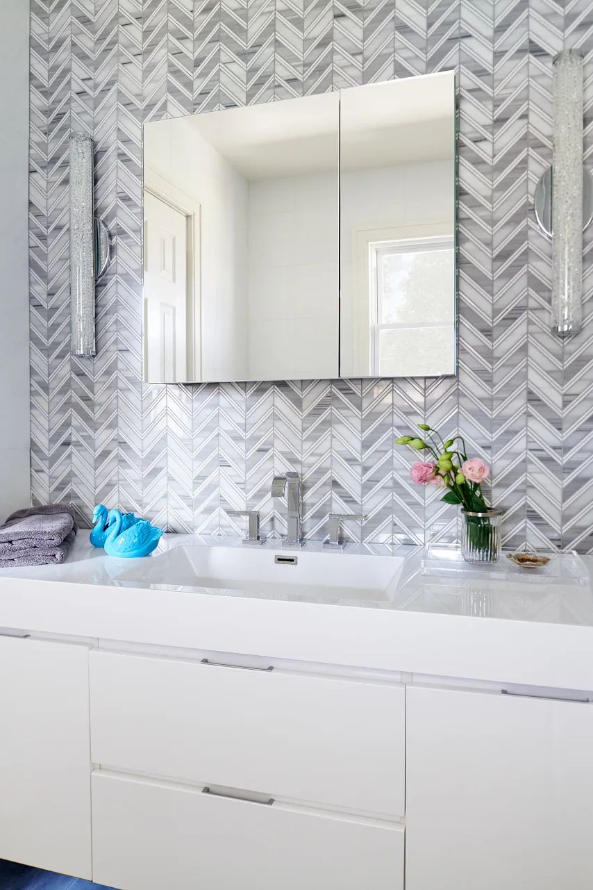 Bathroom with double sink vanity, large mirror, herringbone backsplash, and decorative items.
