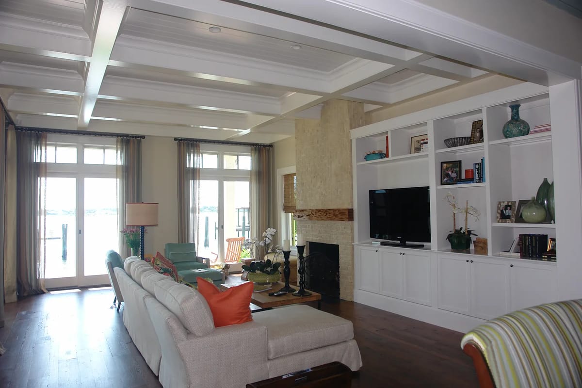 Living room with white sofa, wooden coffee table, green chairs, stone fireplace, and large windows.