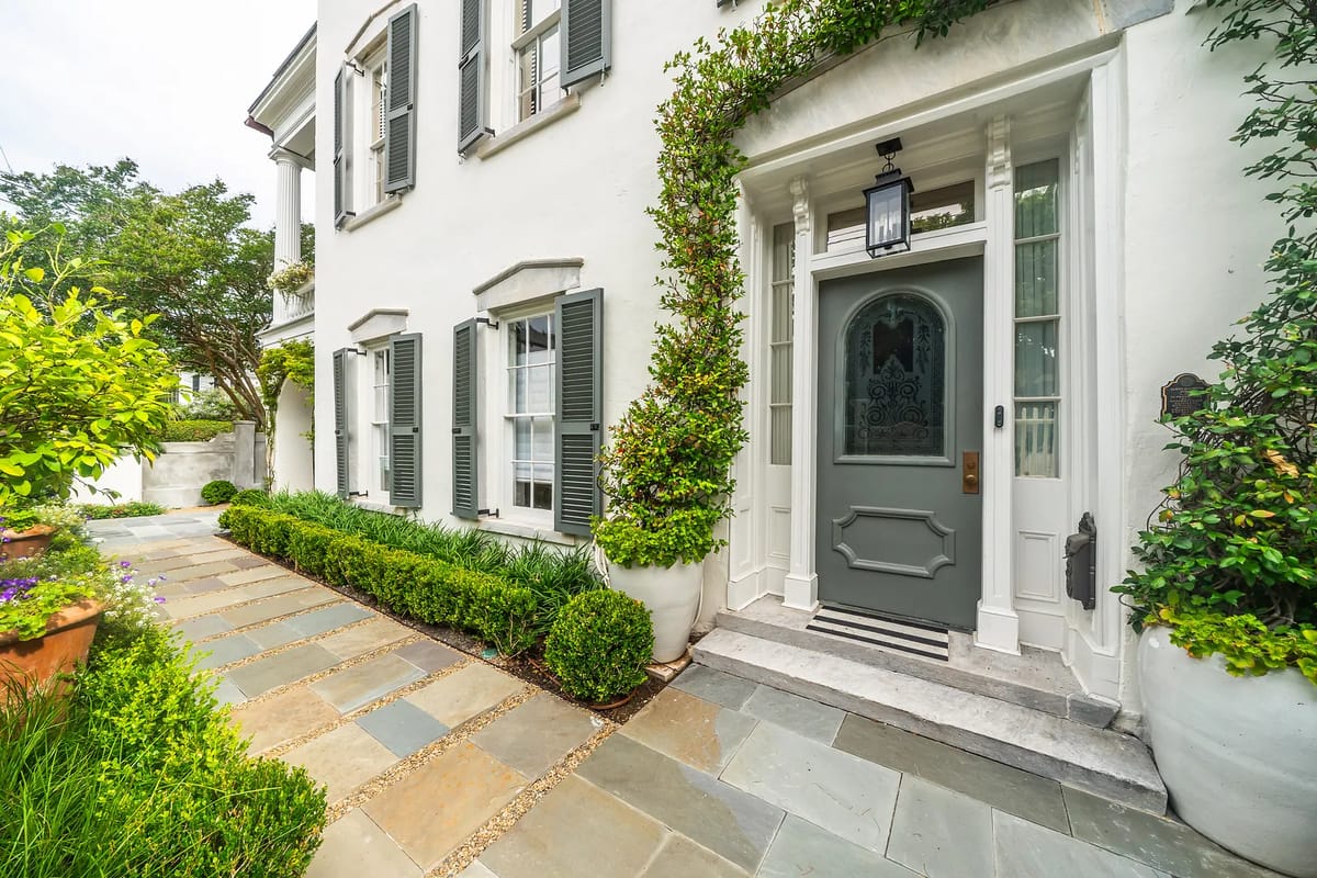 Exterior front view with flagstone pathway, shrubs, flower pots, and a gray entry door framed by columns.