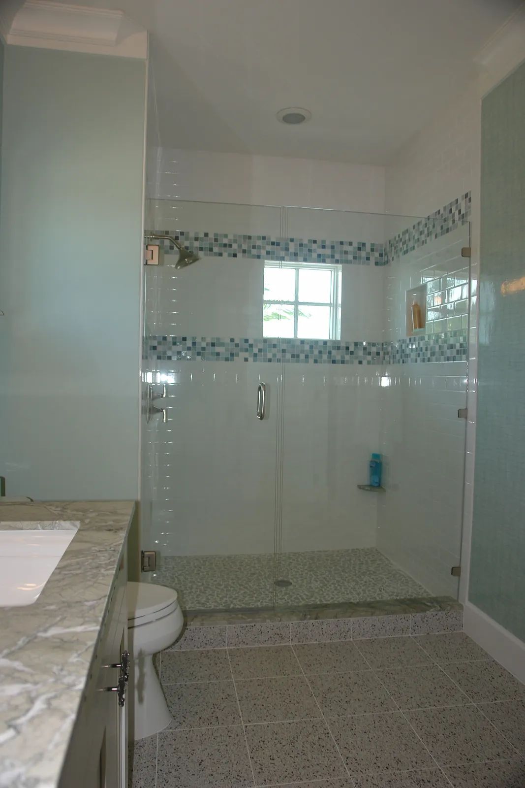 Bathroom with glass shower enclosure, tiled floor, white toilet, marble countertop, and light green walls.
