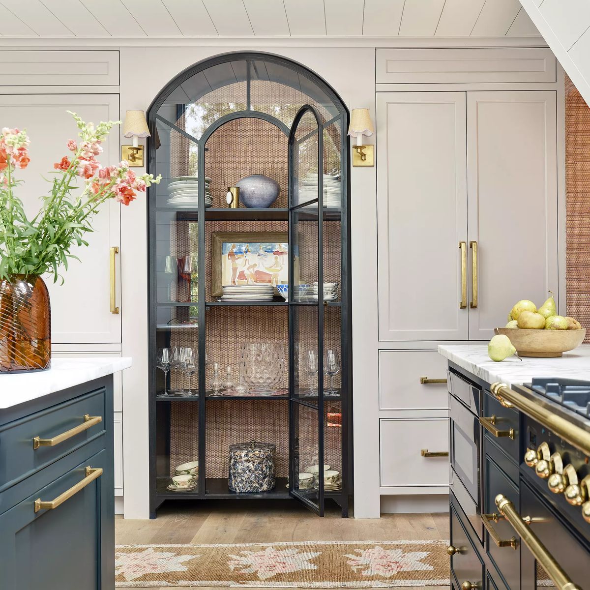Kitchen with glass-front cabinet, light gray cabinetry, white countertop, and floral vase.