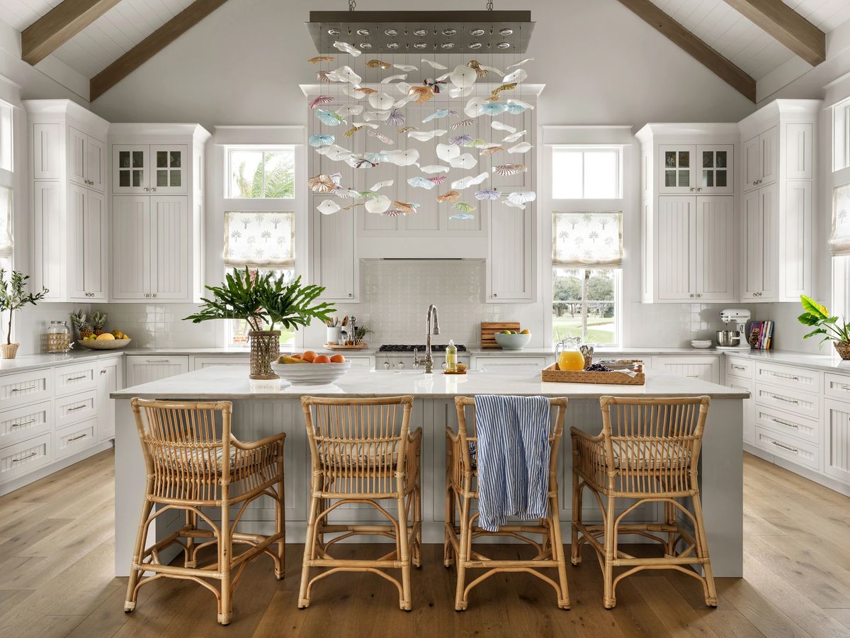 Kitchen with white cabinetry, marble island, rattan bar stools, plants, and a decorative fish installation.