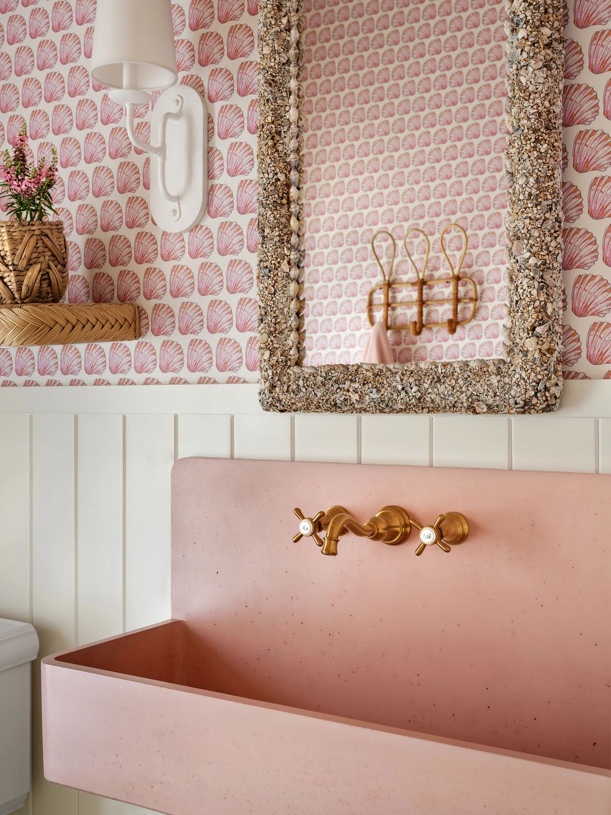 Powder room with pink sink, brass faucets, patterned wallpaper, and decorative mirror.