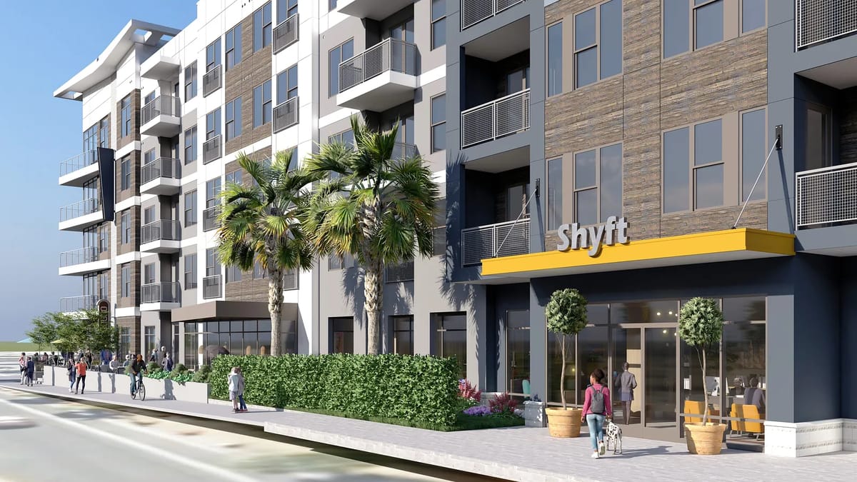 Exterior front of a building with balconies, landscaping, and a sign that reads 'Shyft'.