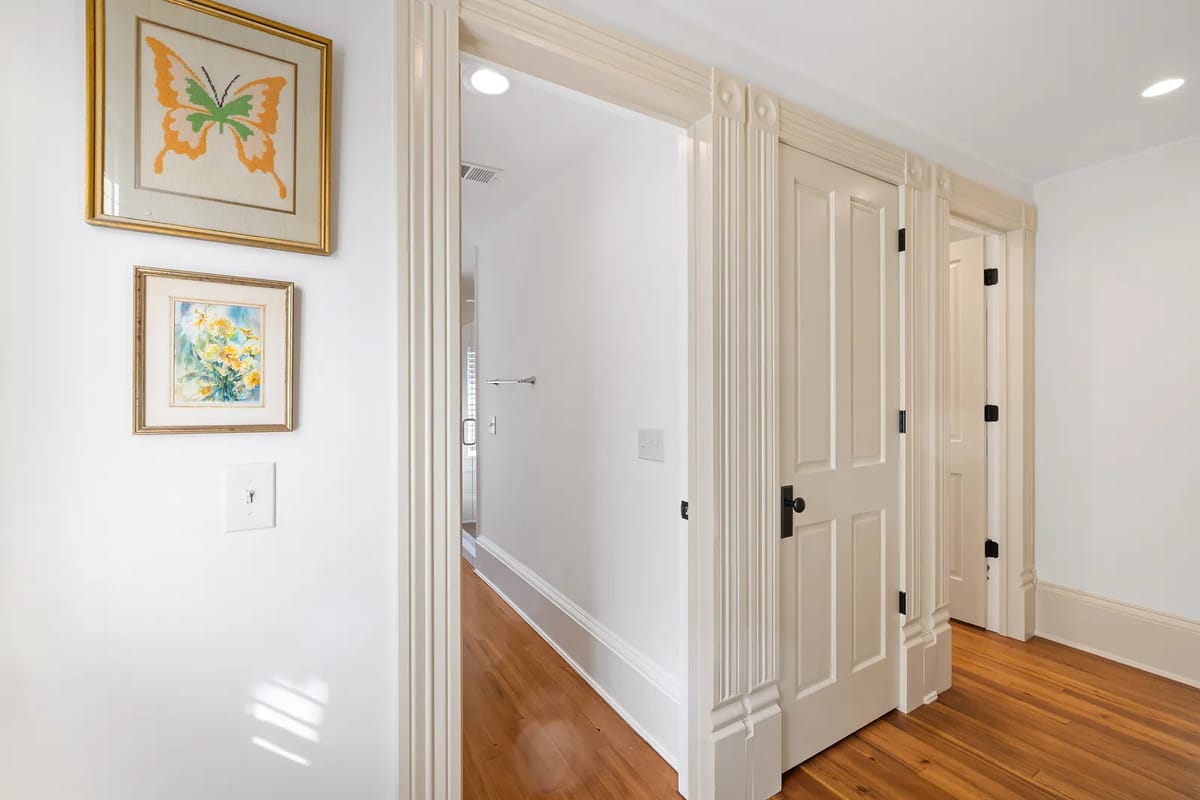 Hallway with white walls, hardwood flooring, framed artwork, and closed doors with black hardware