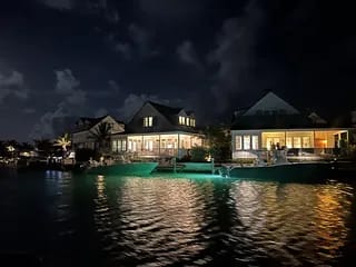 Waterfront property at night with large windows, deck, and outdoor seating.