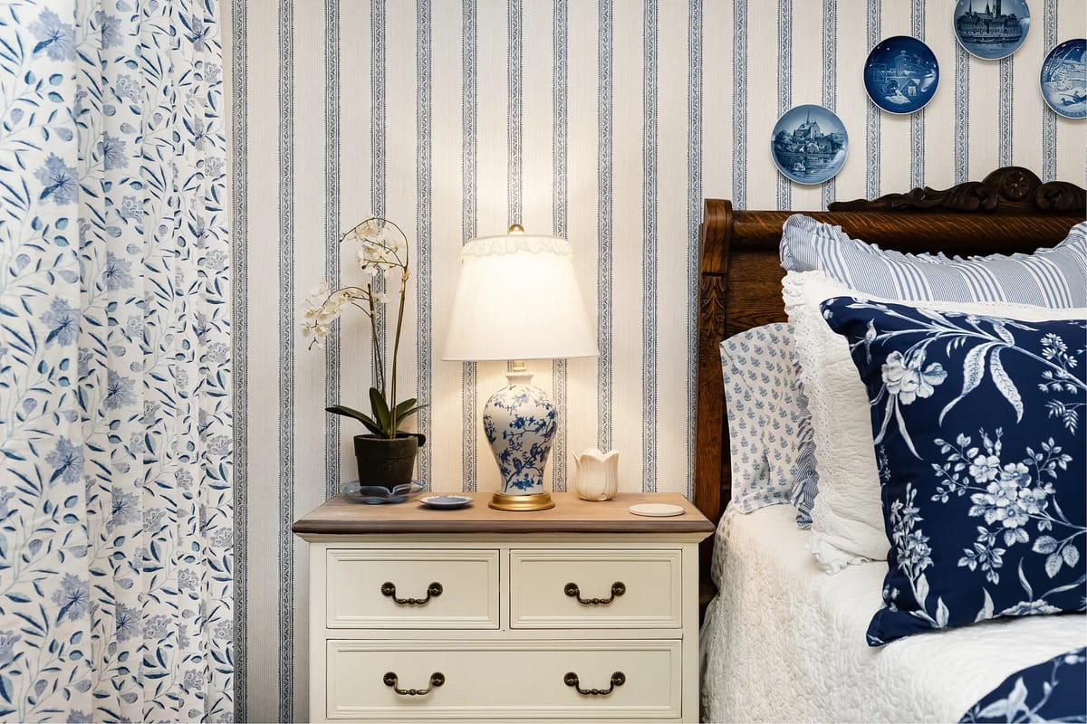 Bedroom with wooden headboard bed, floral bedding, bedside table, lamp, and decorative plates.