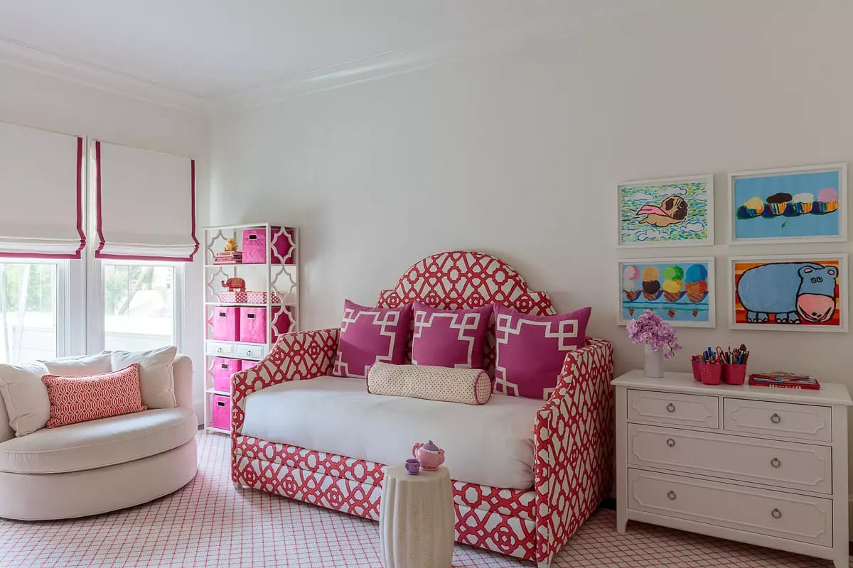 Bedroom with patterned daybed, round chair, colorful storage unit, artworks, and large windows with shades.