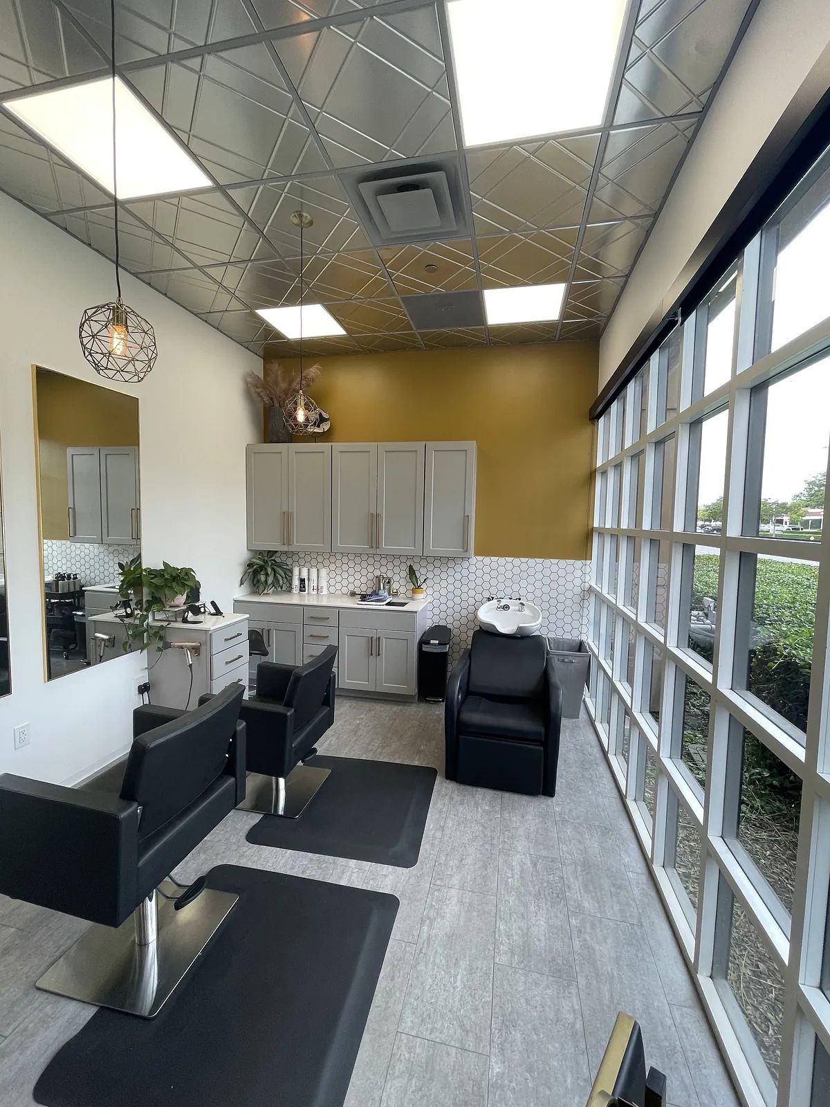 Salon space with black chairs, gray cabinetry, granite countertop, large windows, and metallic ceiling.