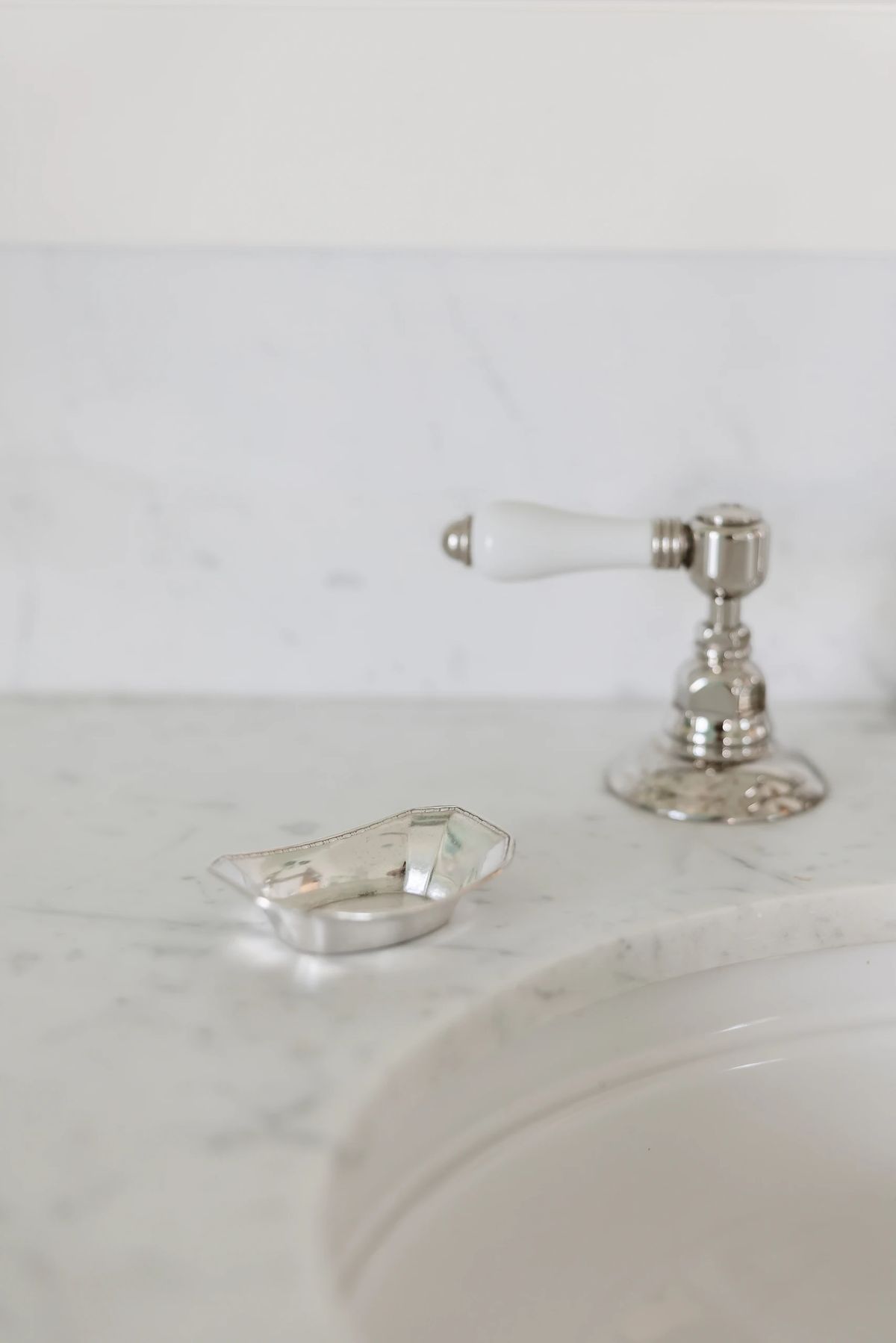 Bathroom countertop with white marble, silver faucet, and decorative dish.