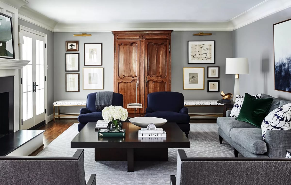 Living room with blue armchairs, gray sofa, dark coffee table, artworks, armoire, and floral centerpiece