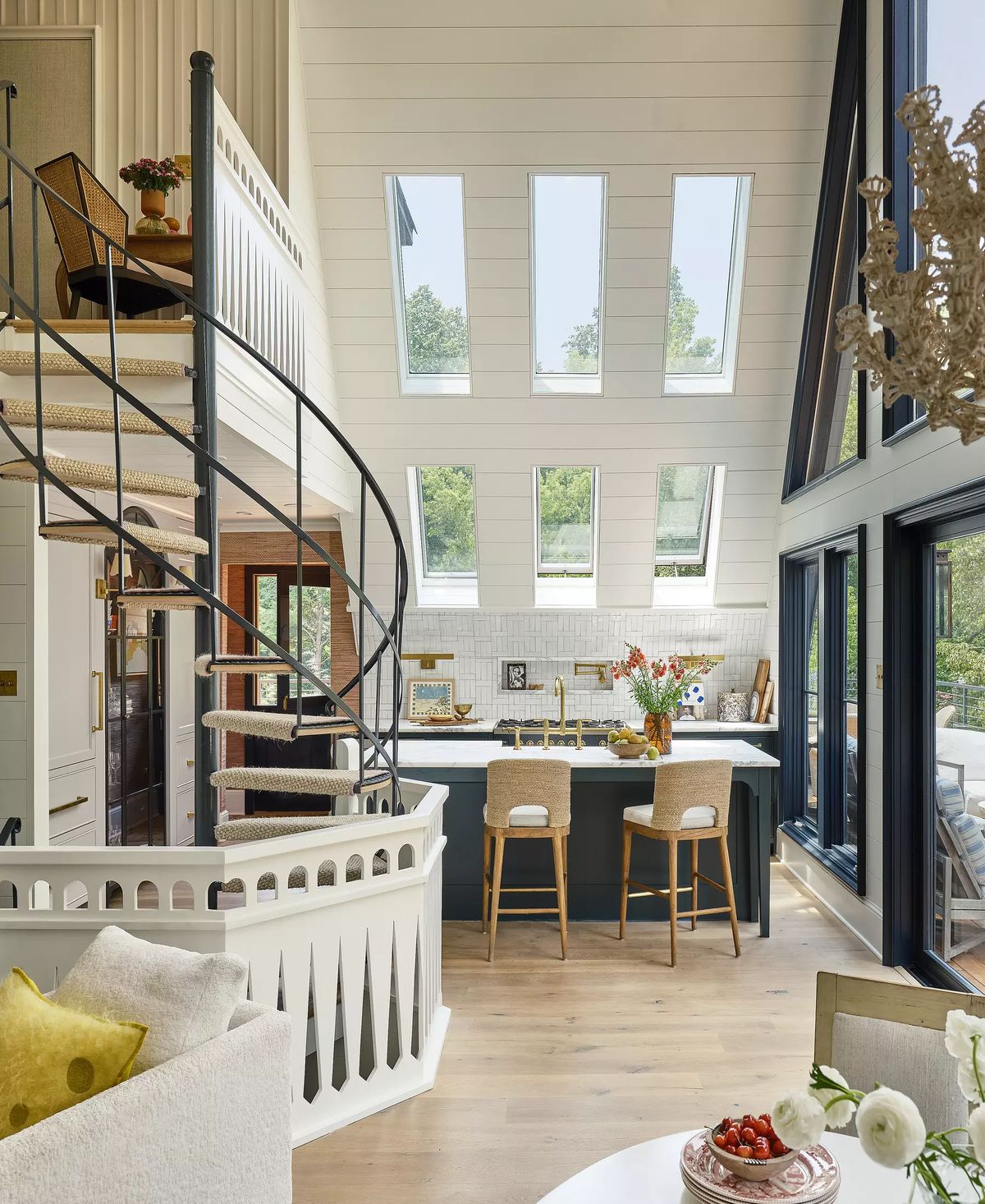 Kitchen with central island, bar stools, light wood cabinetry, white backsplash, and large windows.