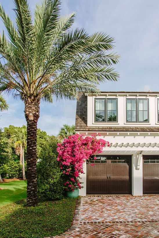 Exterior front view with brick driveway, garage, palm trees, and bougainvillea.