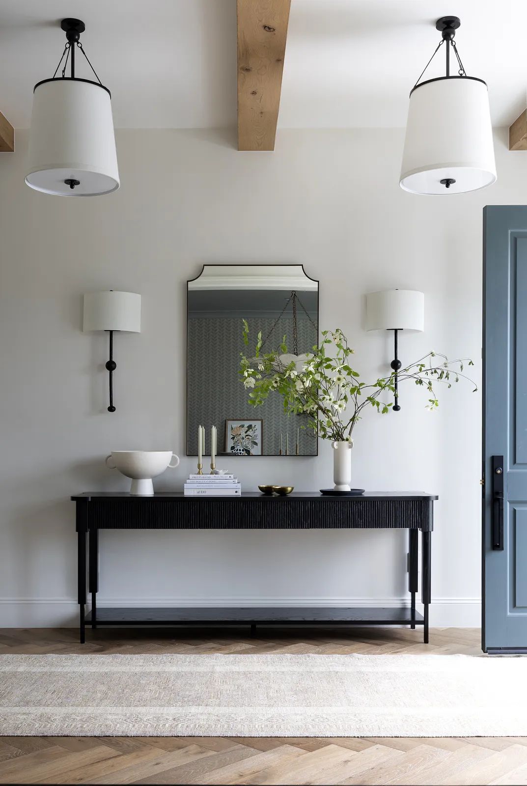 Foyer with black console table, large mirror, vase with branches, and wooden beams on the ceiling