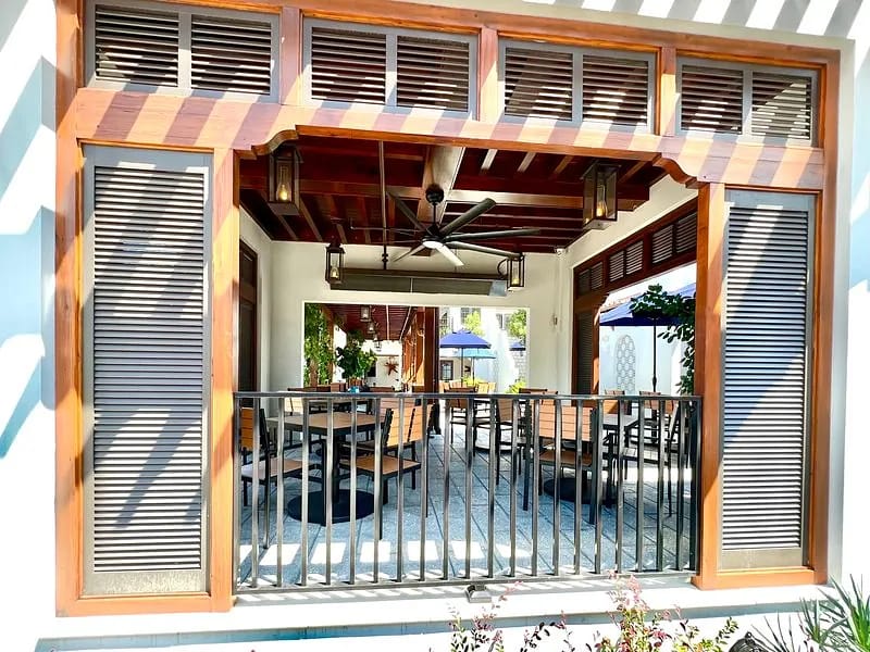 Outdoor space with wooden framing, dining tables, a ceiling fan, and greenery.