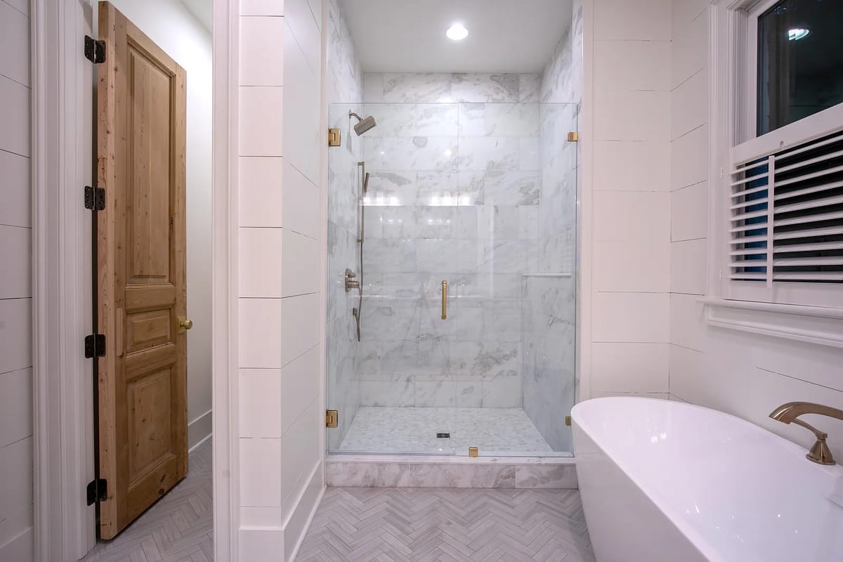 Bathroom with glass shower, freestanding tub, marble walls, and herringbone tiled floor