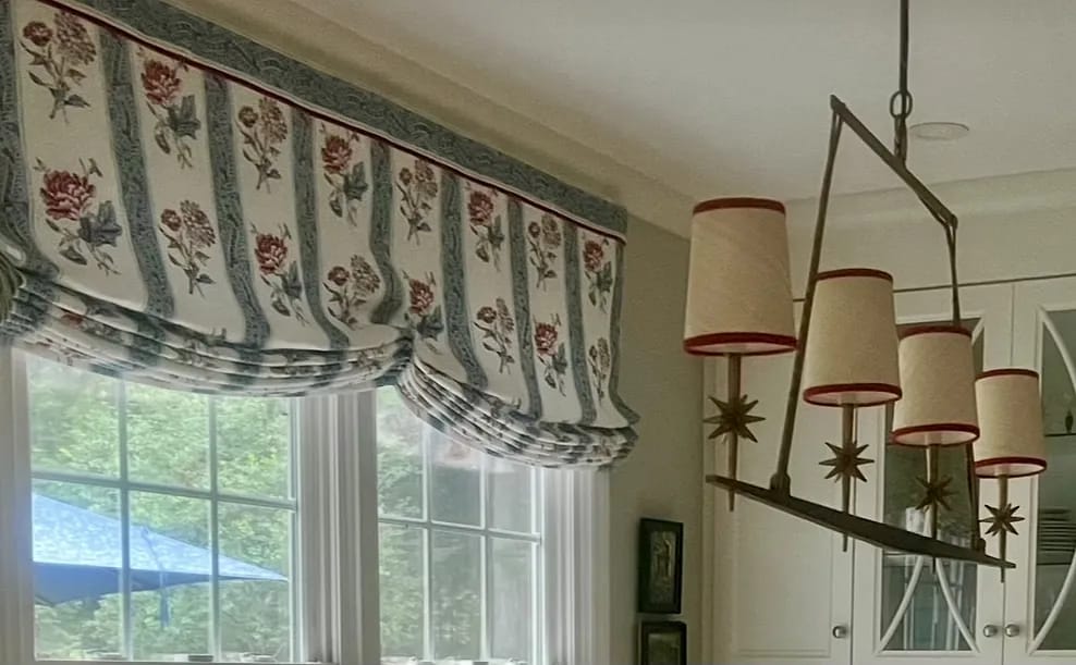 Kitchen with floral window treatment, large windows, light cabinetry, and a ceiling fixture with five shades