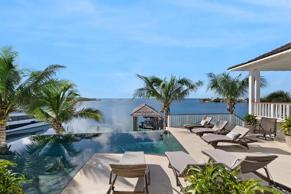 Patio with infinity pool, lounge chairs, palm trees, and gazebo overlooking the ocean.