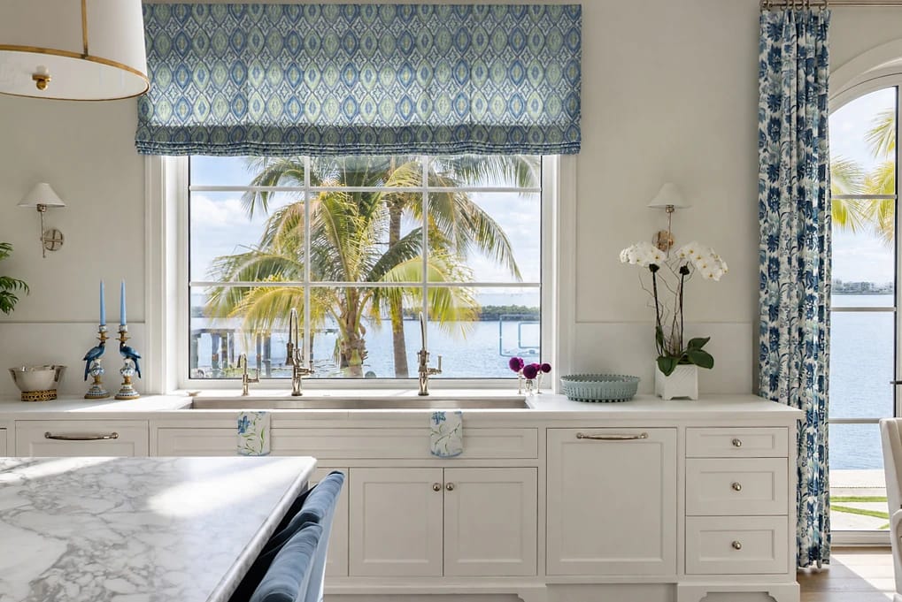 Kitchen with white cabinetry, marble countertop, blue valance, bar stool, and view of palm trees.