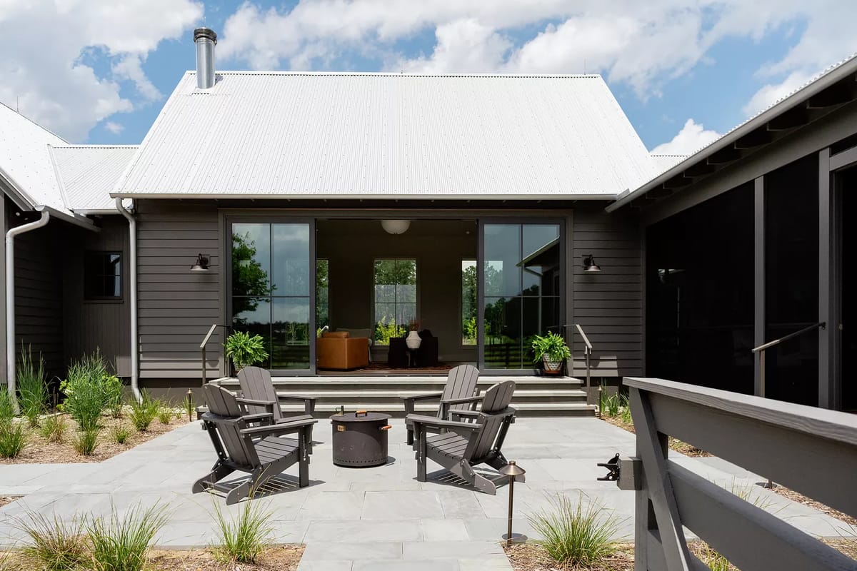 Patio with four black Adirondack chairs around a fire pit and large sliding doors leading into a living space.