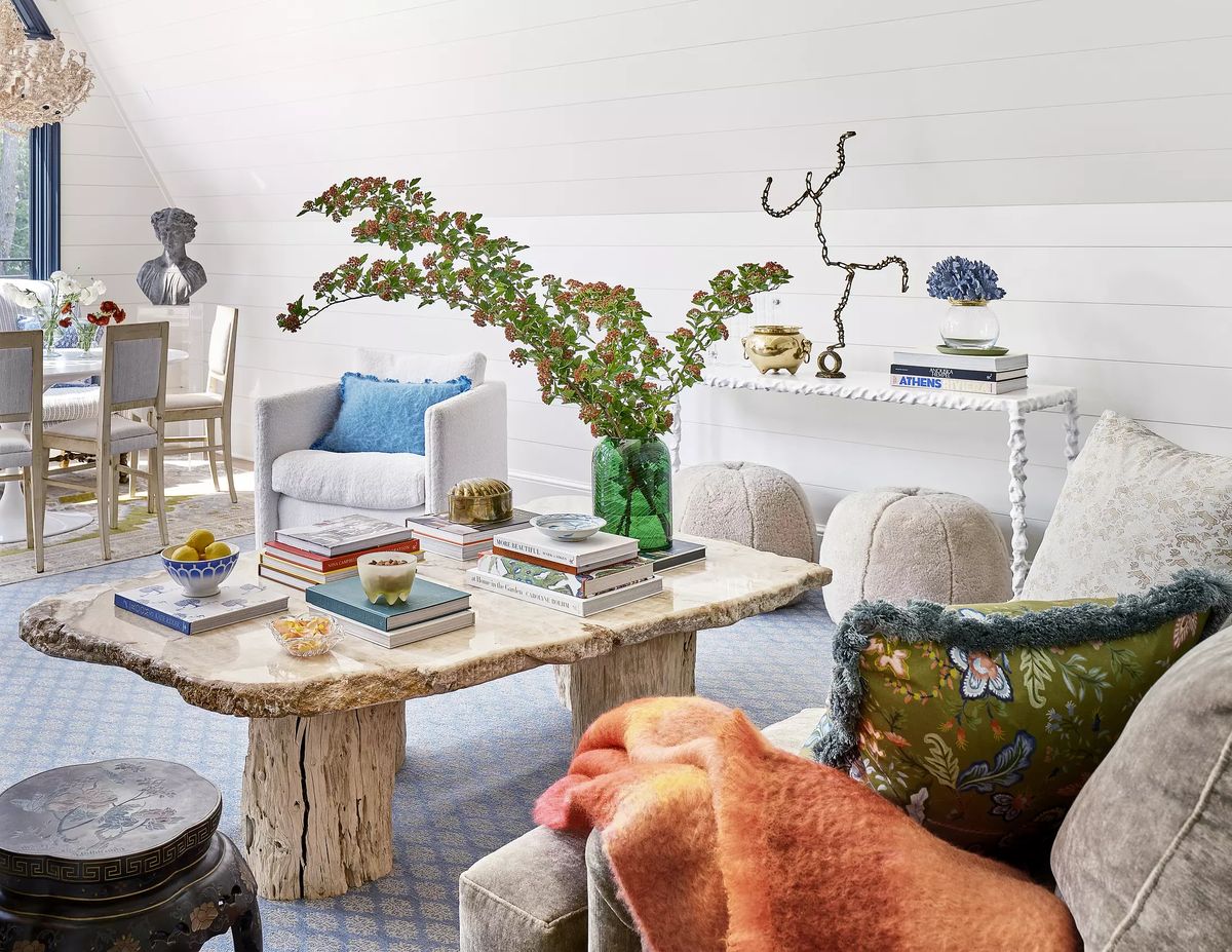 Living room with textured coffee table, white armchair, cushions, decorative vases, and stacked books.