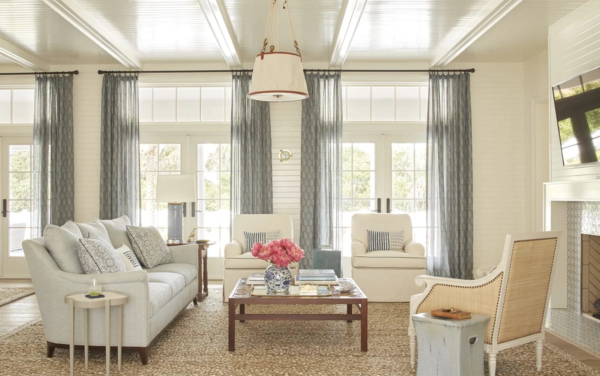 Living room with gray sofa, armchairs, coffee table, area rug, large windows, and a mounted television over a fireplace