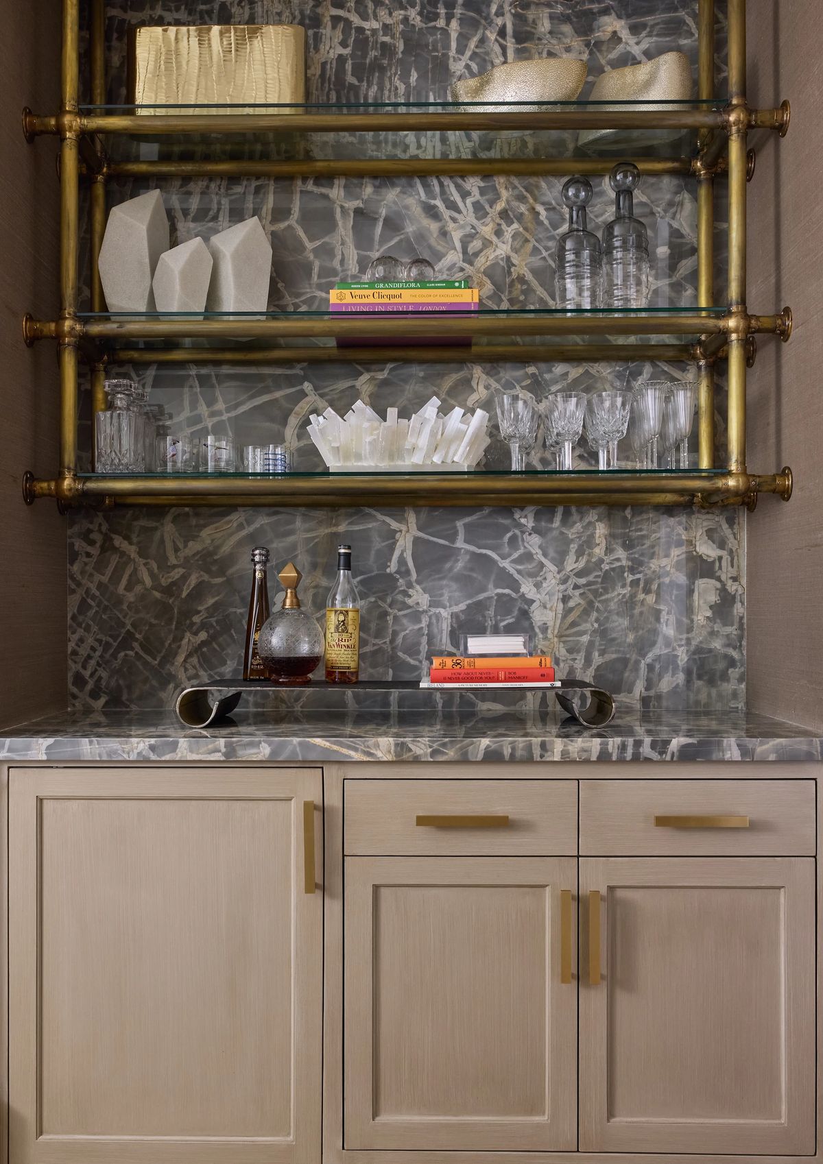 Butler's pantry with brass shelves, marble countertop, bottles, and decorative glassware.