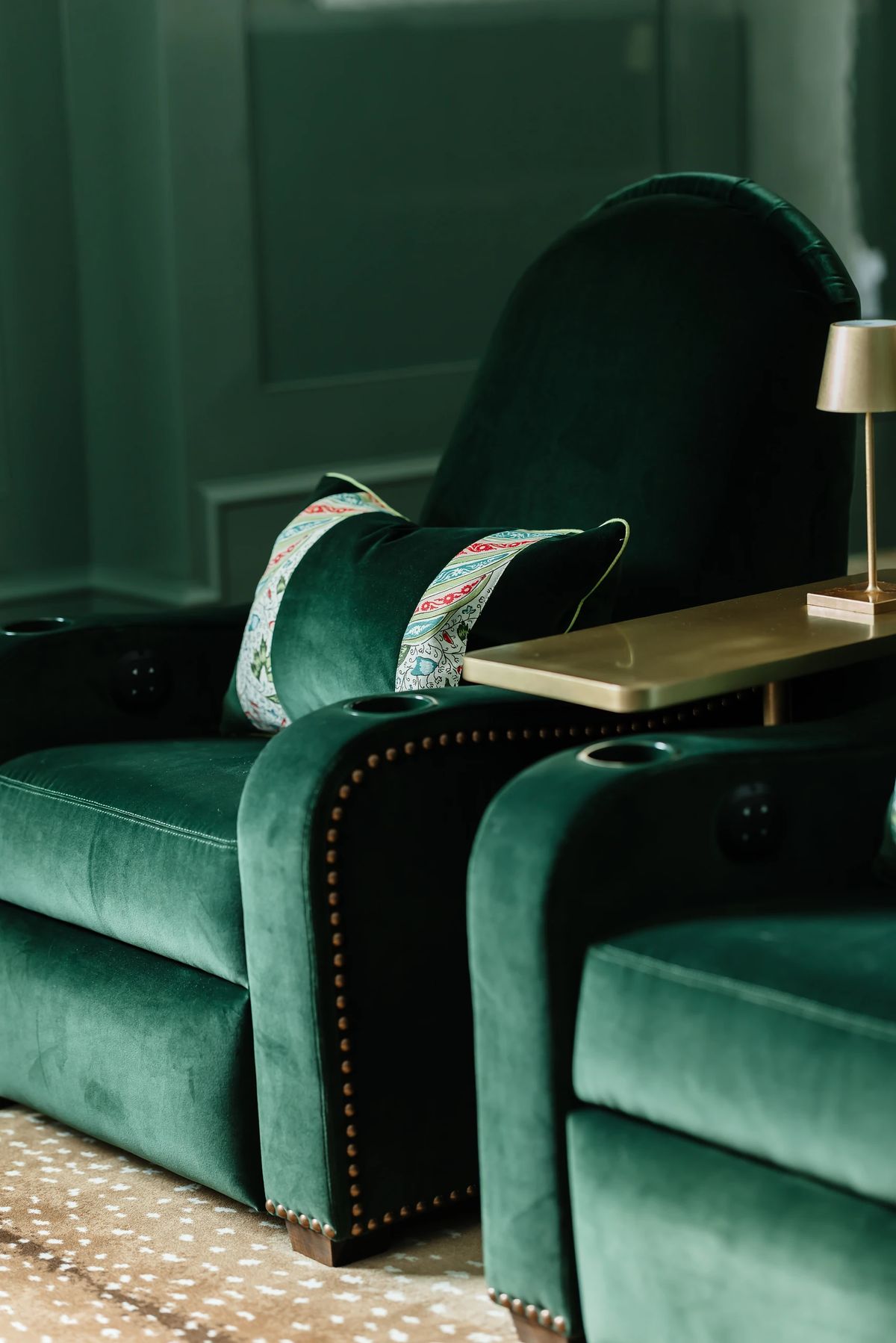 Living room with green velvet recliners, side table, and patterned cushion on a light area rug