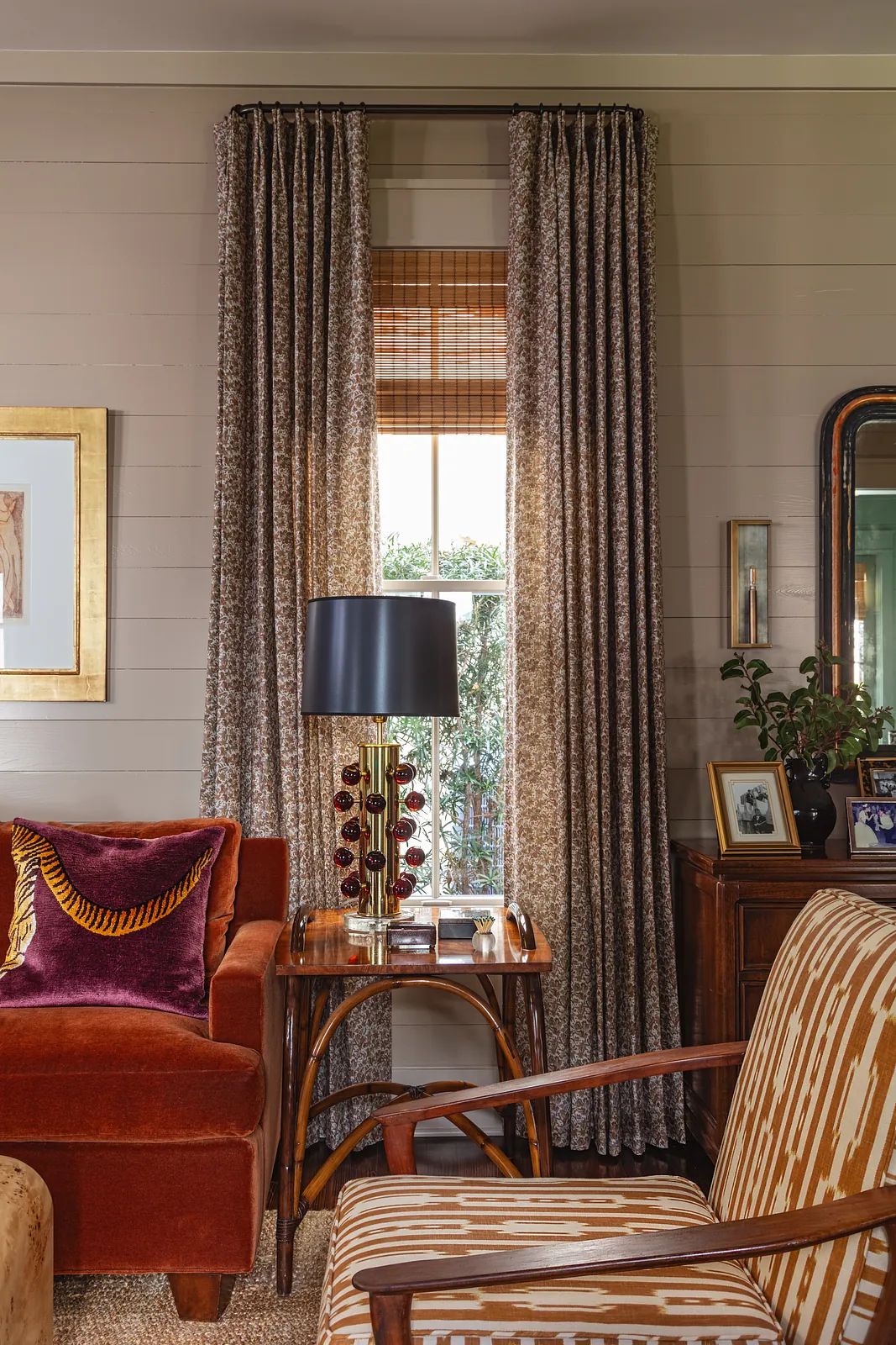 Living room with brown sofa, striped chair, side table, lamp, window, and floral curtains