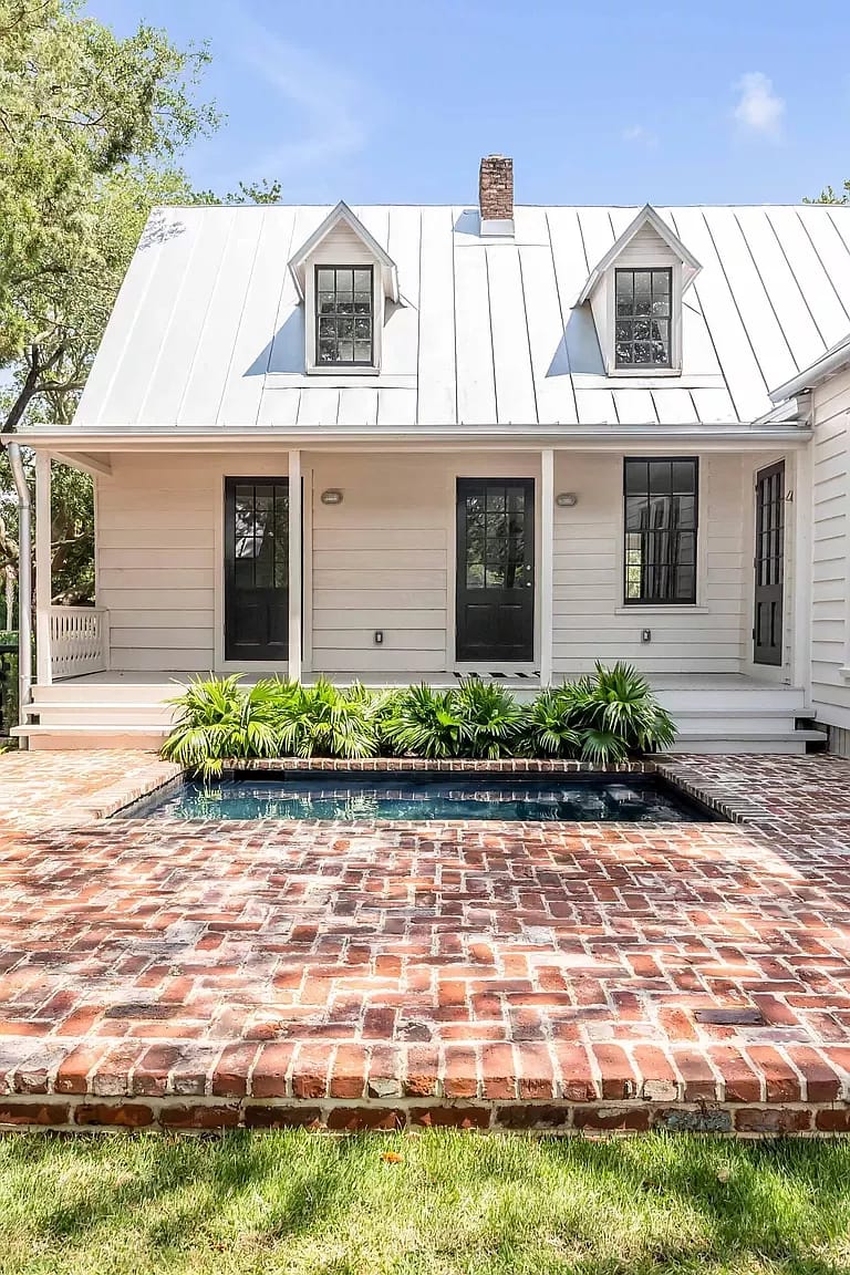 Exterior rear view with brick patio, small pool, greenery, and house with metal roof and dormer windows