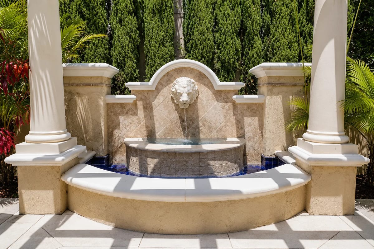 Garden area with stone fountain, lion head, blue tile accents, and landscaped plants on a paved patio.