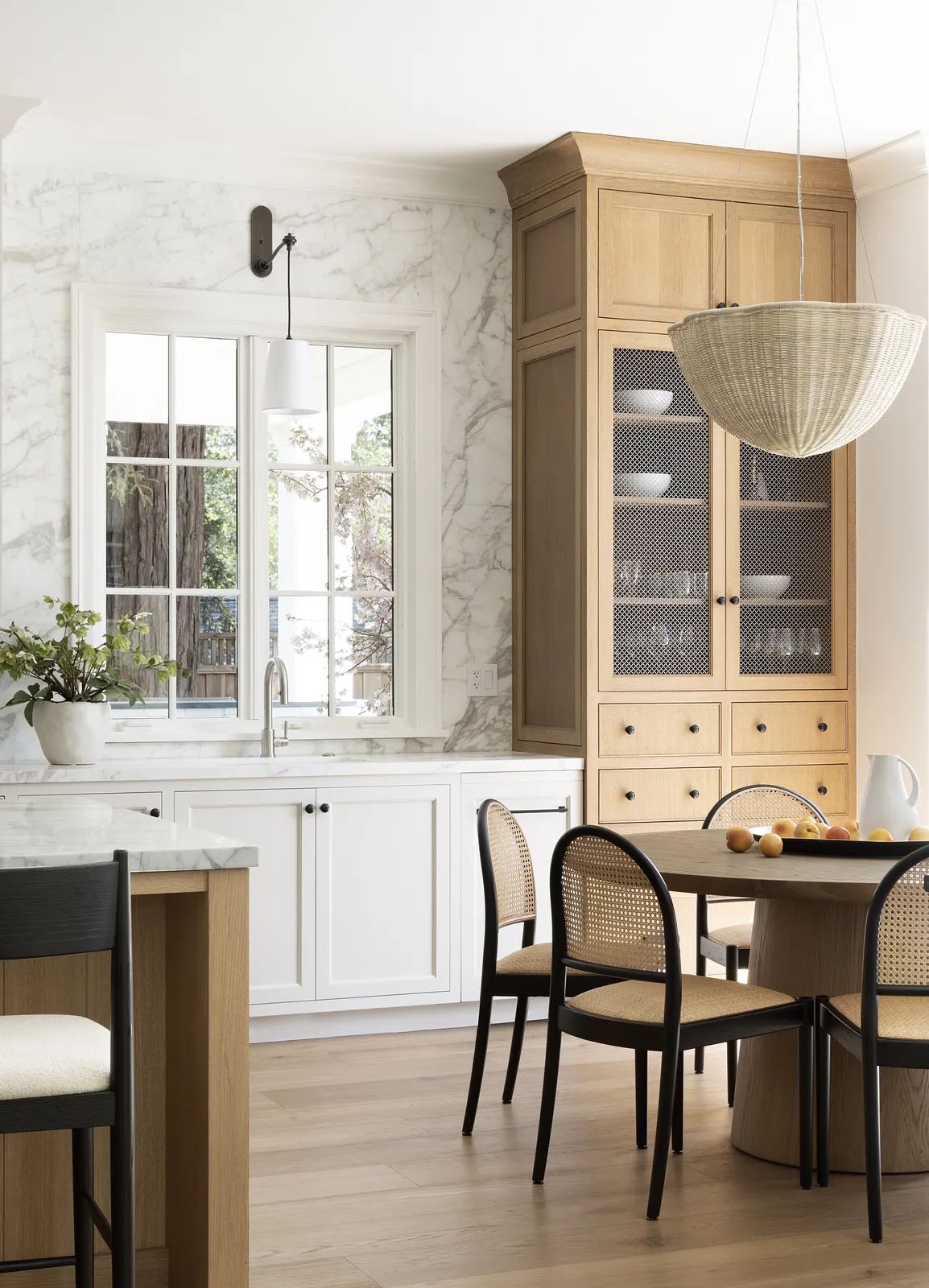 Kitchen with marble backsplash, wooden cabinets, black dining chairs, round table, and a pendant light.