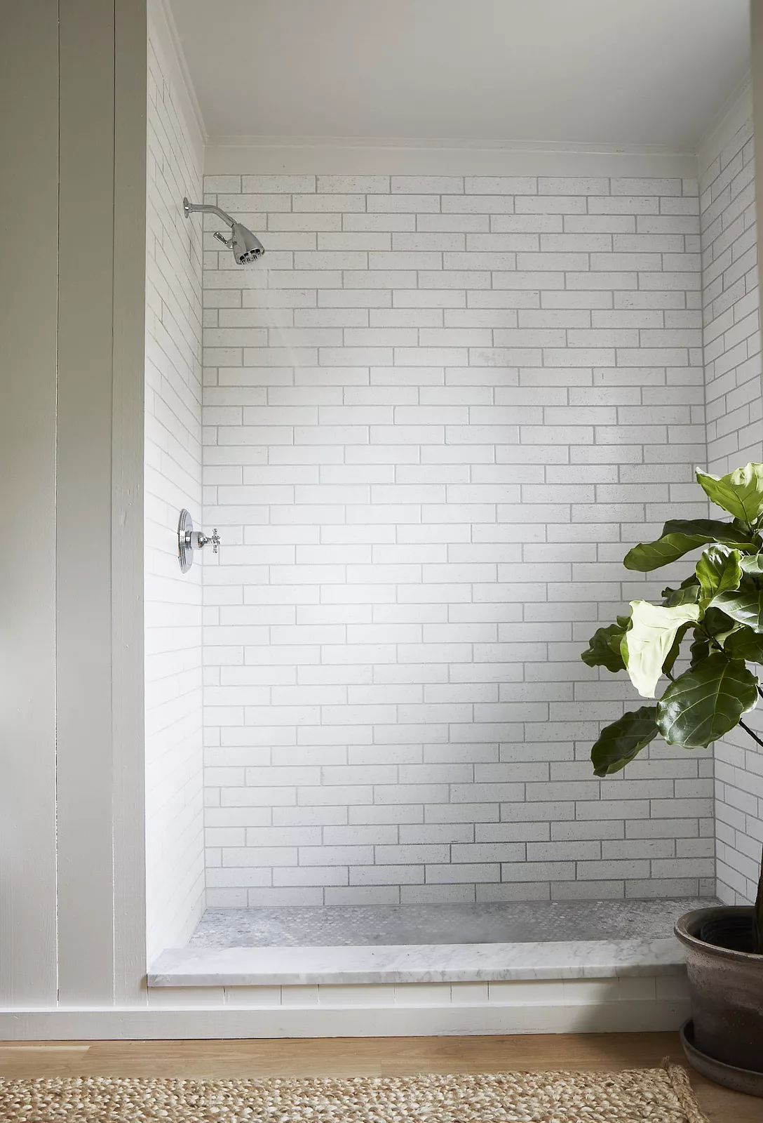 Bathroom with white subway tile shower, marble floor, and large potted plant