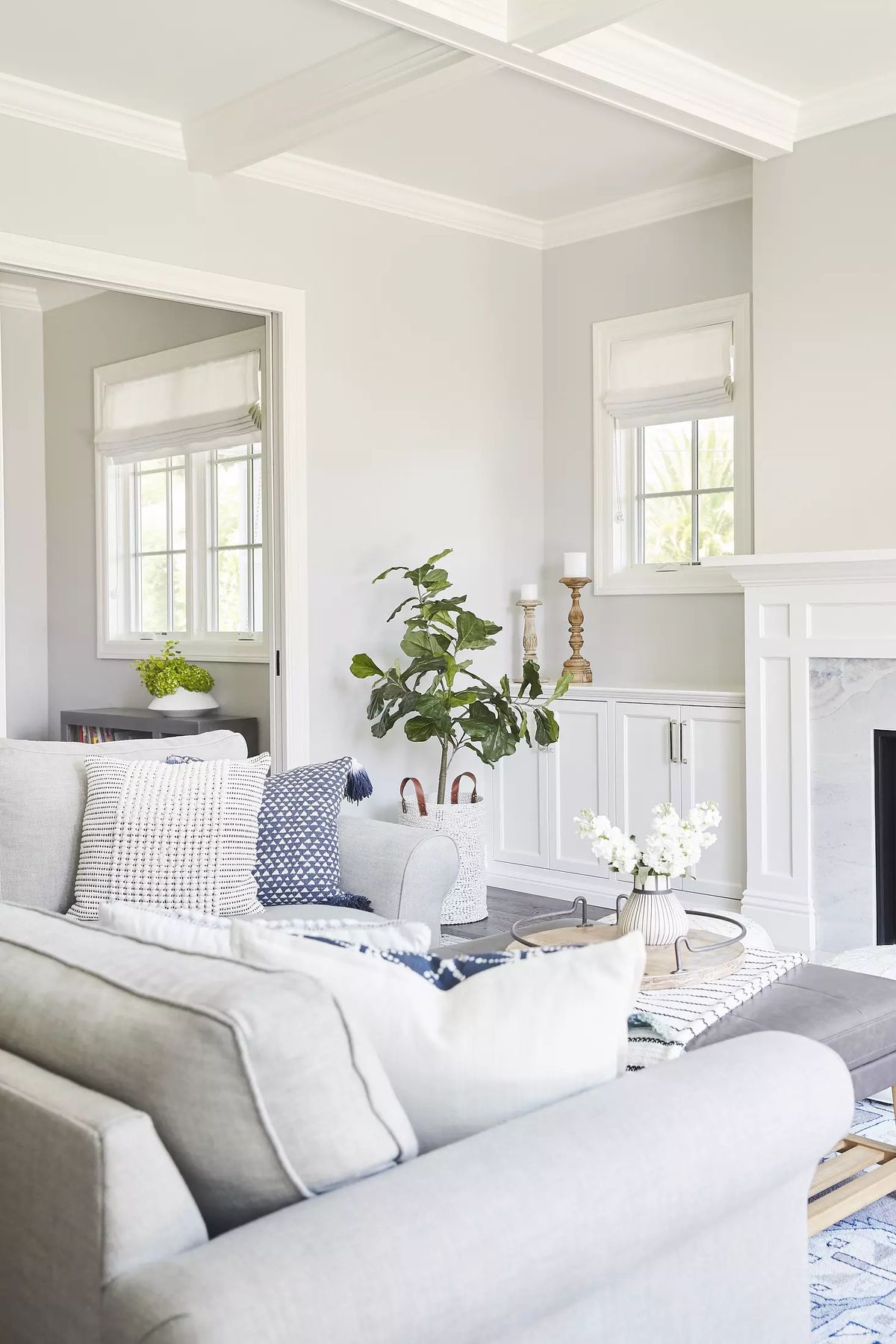 Living room with gray sofa, low coffee table, plant, built-in cabinet, large windows, and white fireplace mantel.