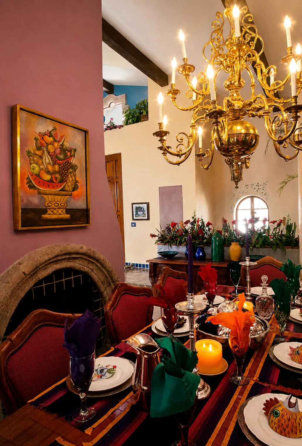 Dining room with a table for eight, colorful goblets, chandelier, painting, and fireplace.