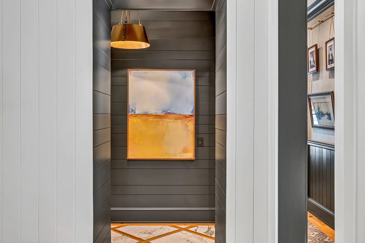 Hallway with gray paneling, abstract painting, patterned tile floor, and pendant light.