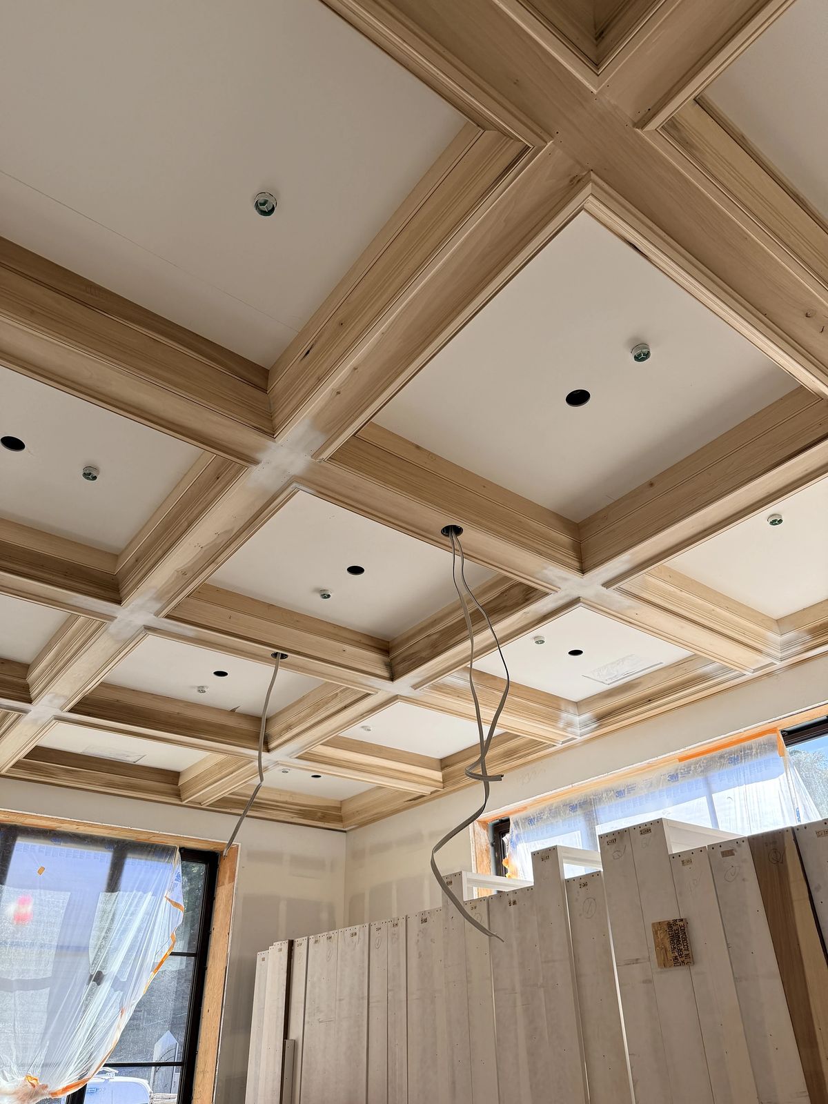 Partially constructed room with a coffered ceiling, unfinished walls, and large windows covered with plastic.