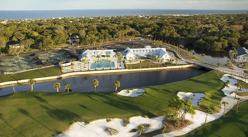 Outdoor landscape with pool, tennis courts, water body, and golf course elements amidst lush greenery.